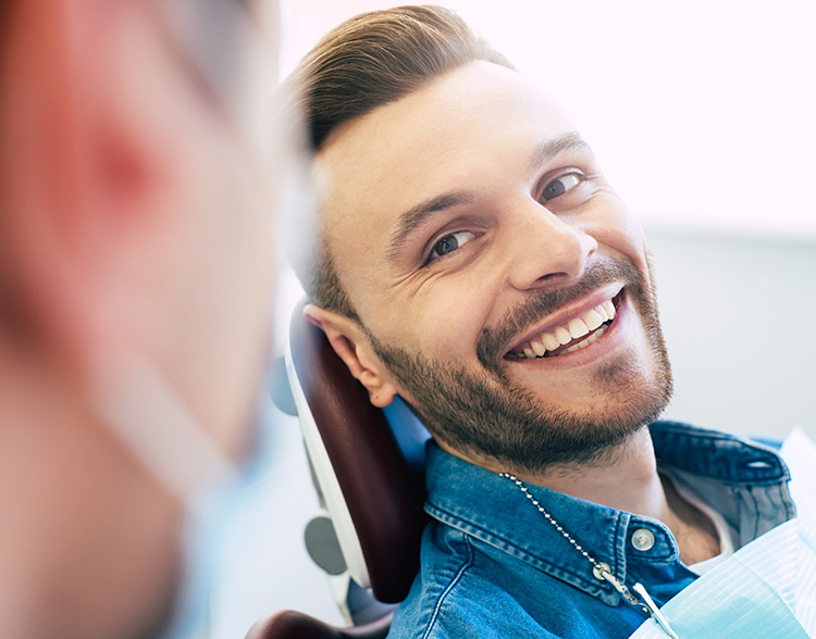 Achieving Safe And Predictable Outcomes Man smiling in dental chair during exam, representing comfortable dental visit and positive patient experience