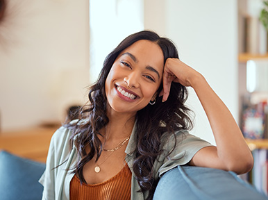 Elevating Your Aesthetics CEREC Woman smiling on couch at home, representing comfortable dental care and confident, healthy smile