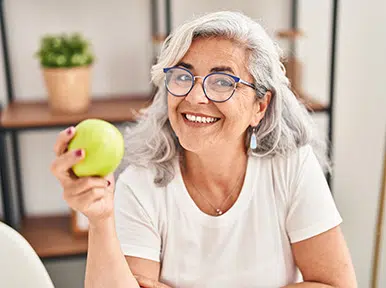 Improving Oral Functionality and Health Full Arch Implants Older woman holding apple and smiling, representing preventive dental care and healthy lifestyle habits